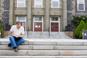 man reading text book sitting on stairs