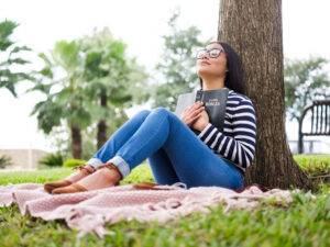 young woman holding bible close under tree